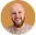 Smiling bald man with a beard wearing a tan shirt against a neutral background.